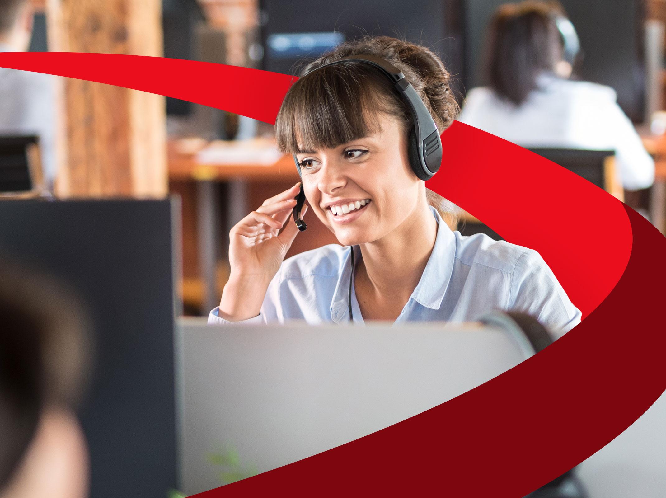 A customer care professional speaking into a headset and smiling.  She is in an office setting.
