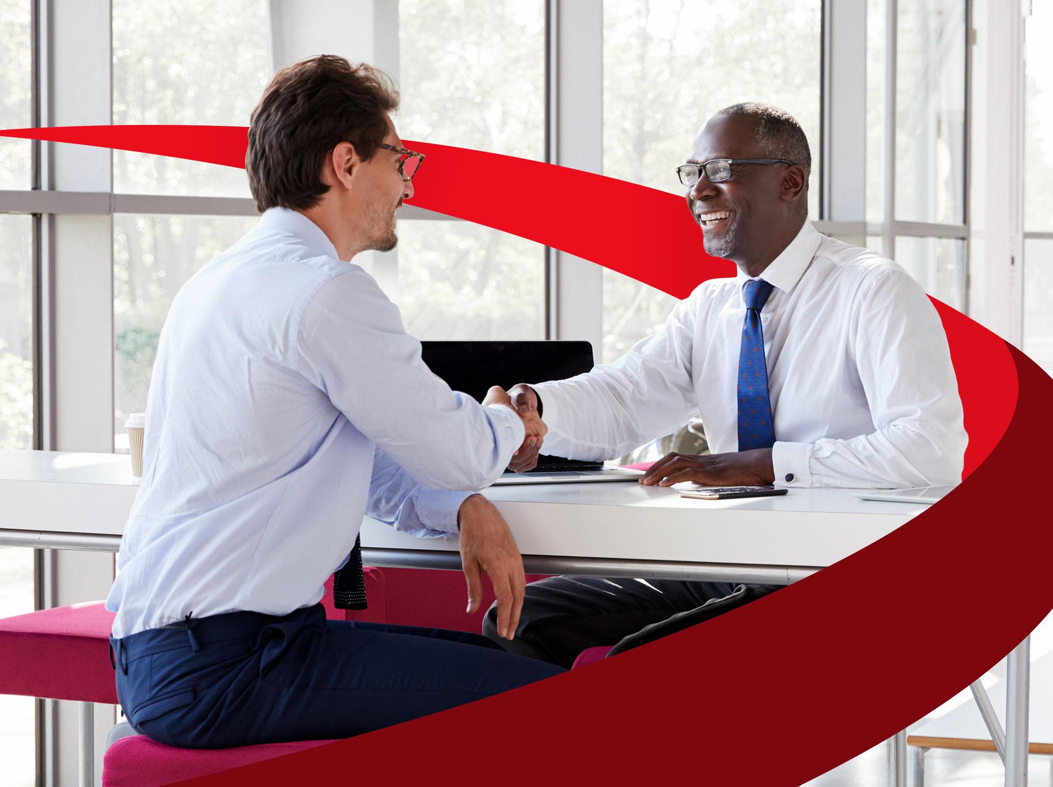 Two business professionals shaking hands across a desk in a business setting.