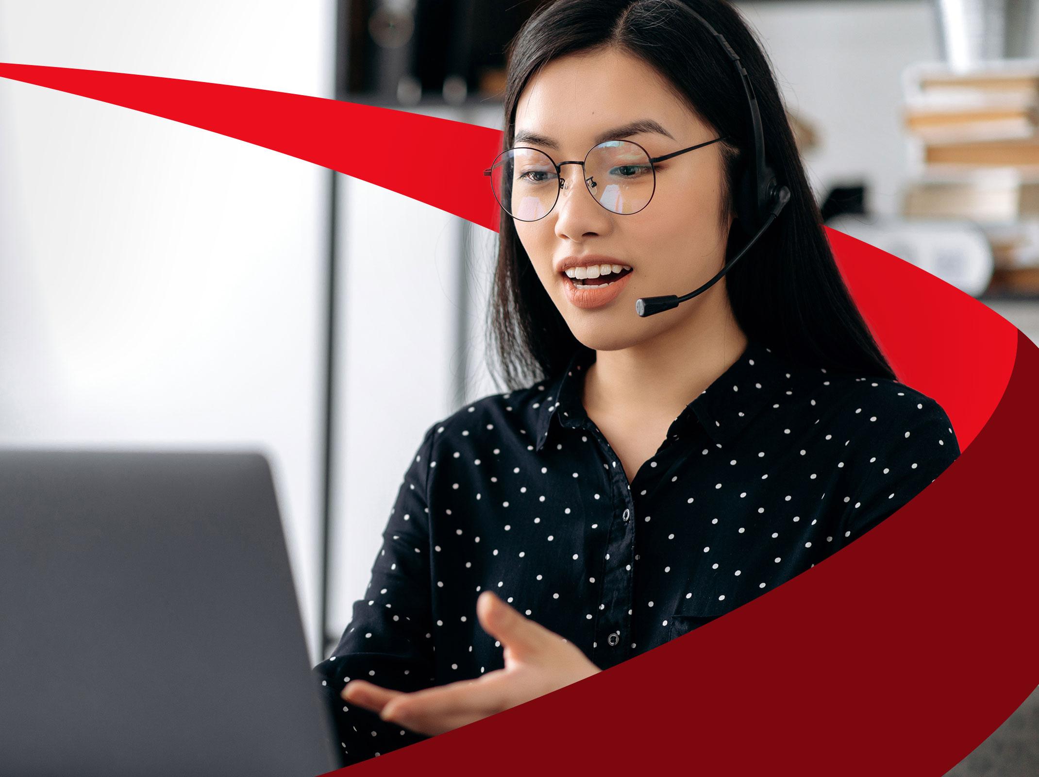 Woman in a customer service role talking on a headset in front of a computer.